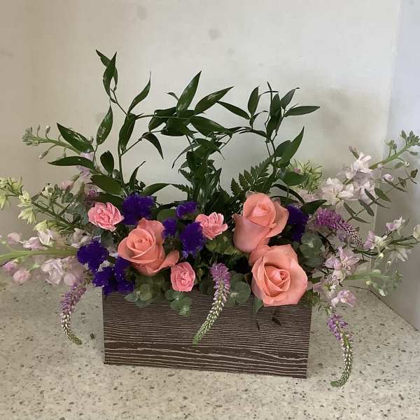 Pink roses and purple flowers arranged in a rectangular wooden box