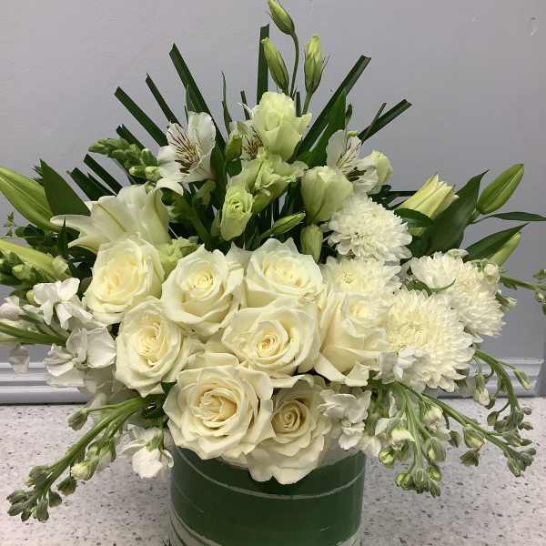 White roses and lilies arranged in a green glass vase