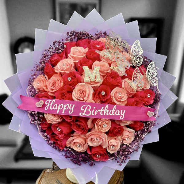 Round bouquet of red and peach roses with birthday ribbon and butterflies wrapped in lavender paper