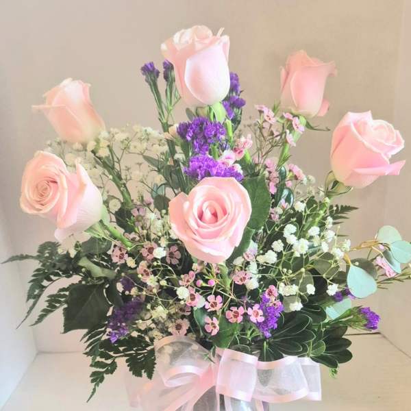 Pink roses and purple filler flowers in a clear vase with a pink ribbon