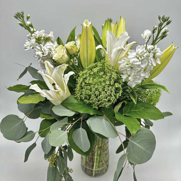 White lilies and green blooms in a glass vase with trailing eucalyptus