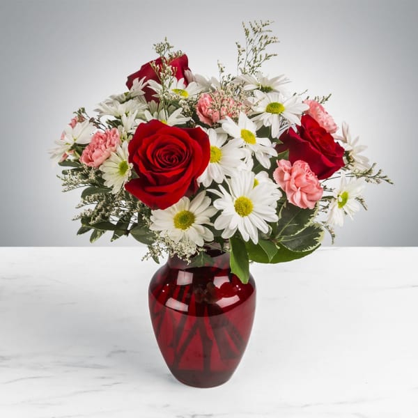 Arrangement of red roses, white daisies, and pink carnations in a red glass vase