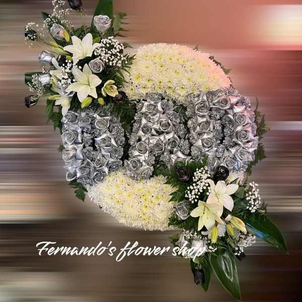 Oval funeral spray reading DAD in silver roses on white mums with white lilies and black accents.