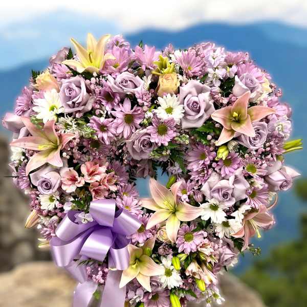 Heart-shaped wreath of pink and lavender flowers with a purple ribbon bow