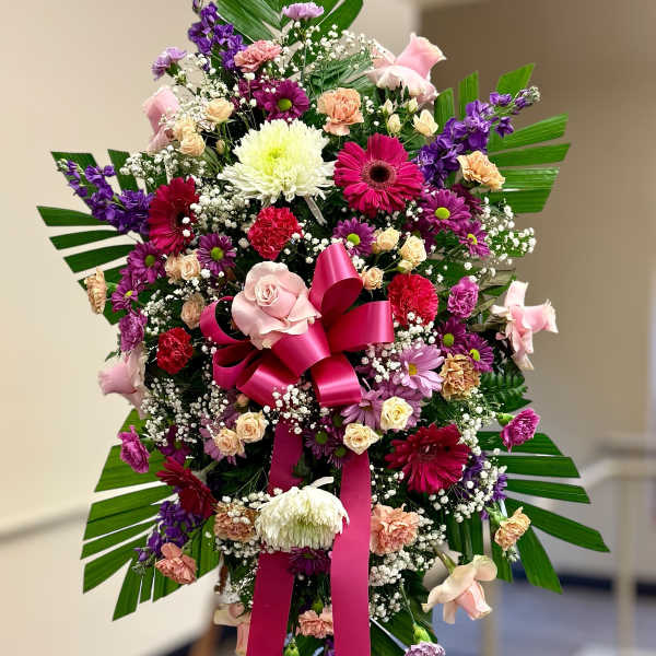 Tall standing spray of pink, purple, and white flowers with a large hot pink bow on an easel