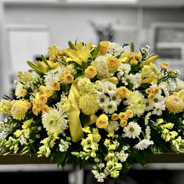 Large yellow and white casket spray with lilies, roses, daisies, and mums on a low rectangular base