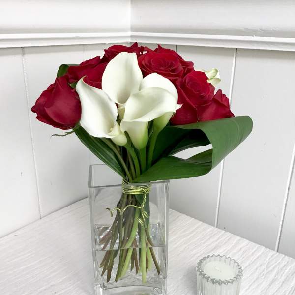 Red roses and white calla lilies in a clear glass vase