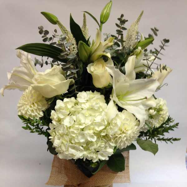 White lilies and hydrangeas arranged in a burlap-wrapped vase