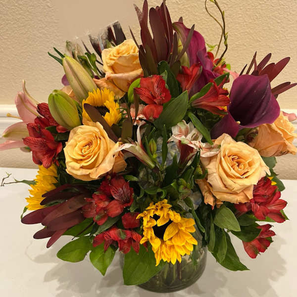 Mixed bouquet of roses, lilies, and sunflowers in a glass vase
