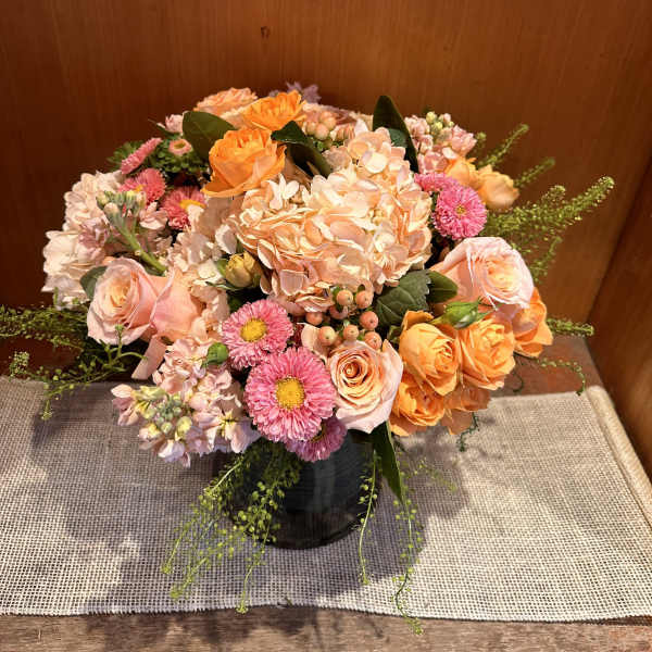 Peach and pink mixed flower arrangement in a dark vase