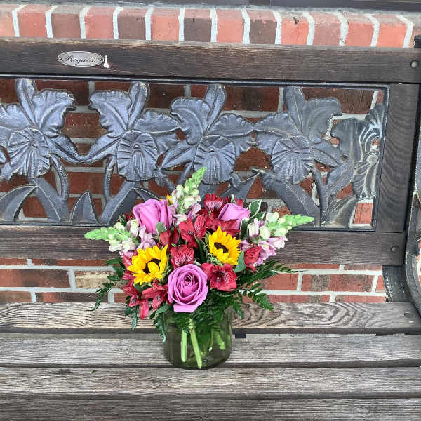 Mixed bouquet of pink roses, sunflowers, and red flowers in a glass vase