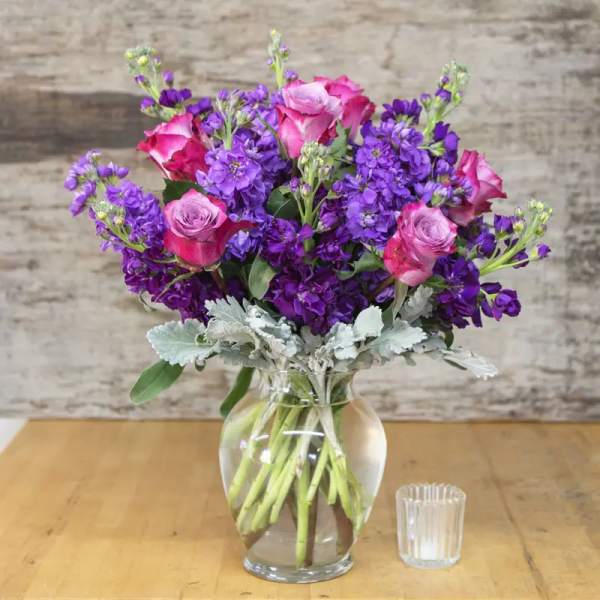 Pink roses and purple flowers arranged in a clear glass vase