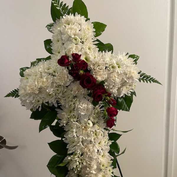 White floral cross arrangement with red roses on a stand
