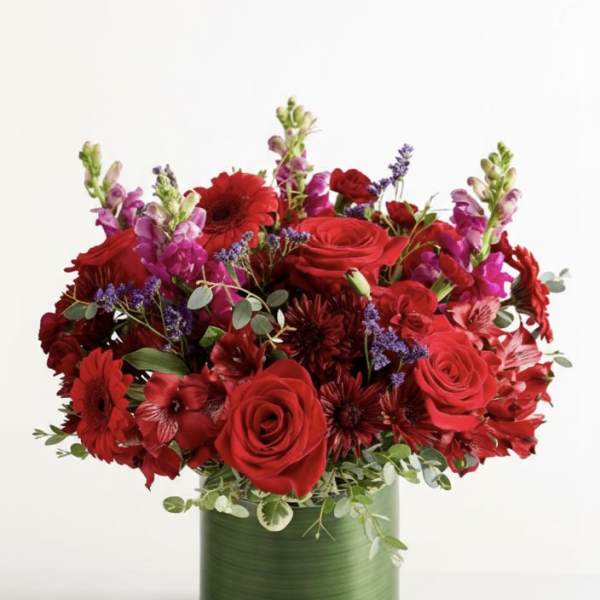 Red roses and mixed red flowers in a green glass vase