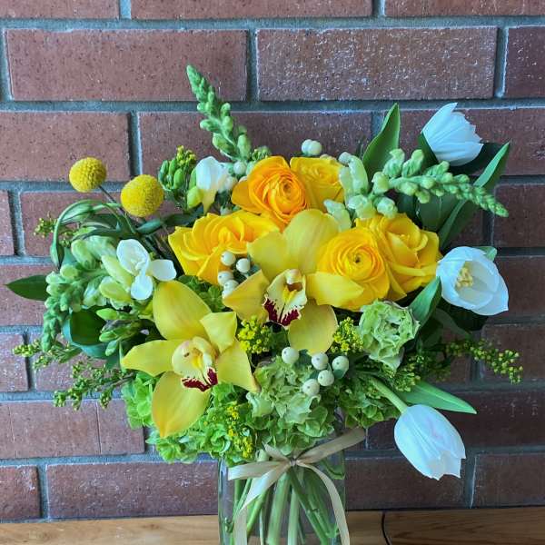 Yellow and white floral arrangement in a glass vase with a ribbon