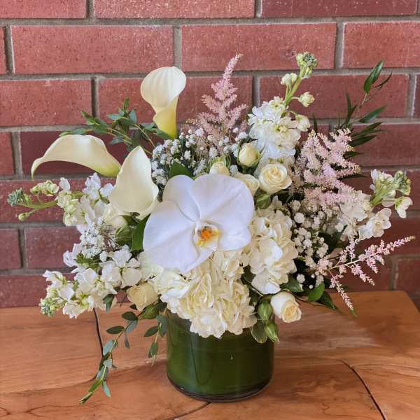White floral arrangement with calla lilies, orchids, and roses in a green vase