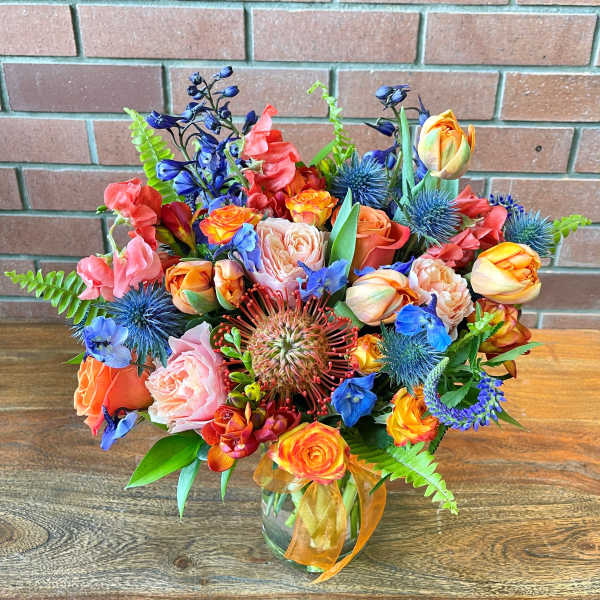 Colorful mixed bouquet in a glass vase with orange, pink, and blue flowers