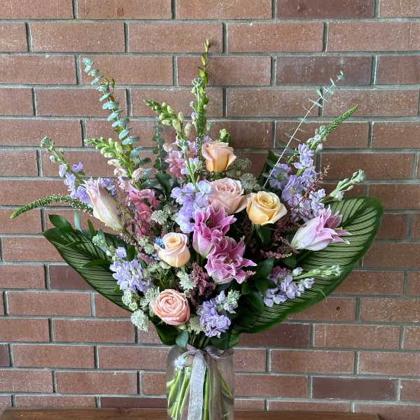 Pastel bouquet of roses, lilies, and purple flowers in a glass vase