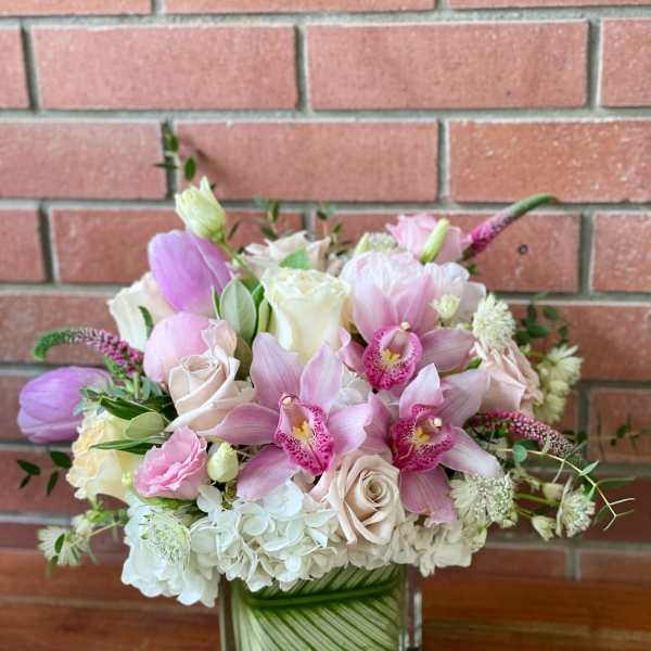 Pink and white bouquet with orchids and roses in a square glass vase