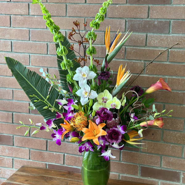 Tropical flower arrangement in a green glass vase with orchids and lilies