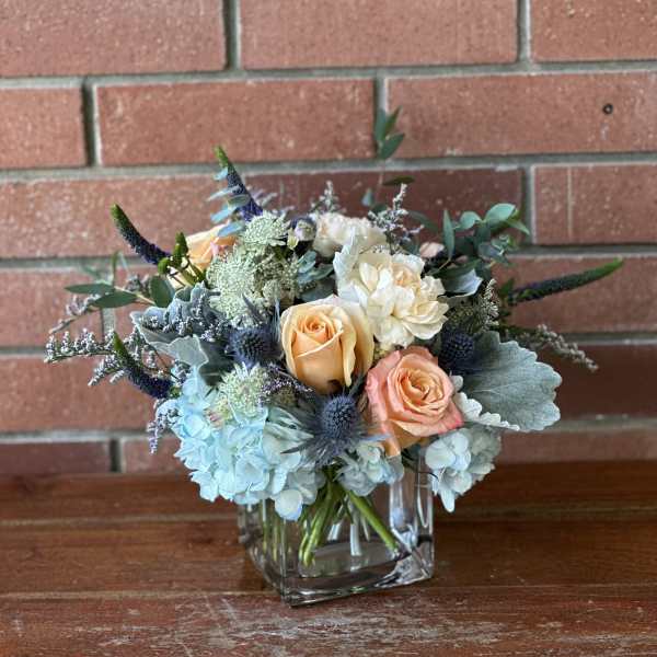 Bouquet of peach and blue flowers in a square glass vase
