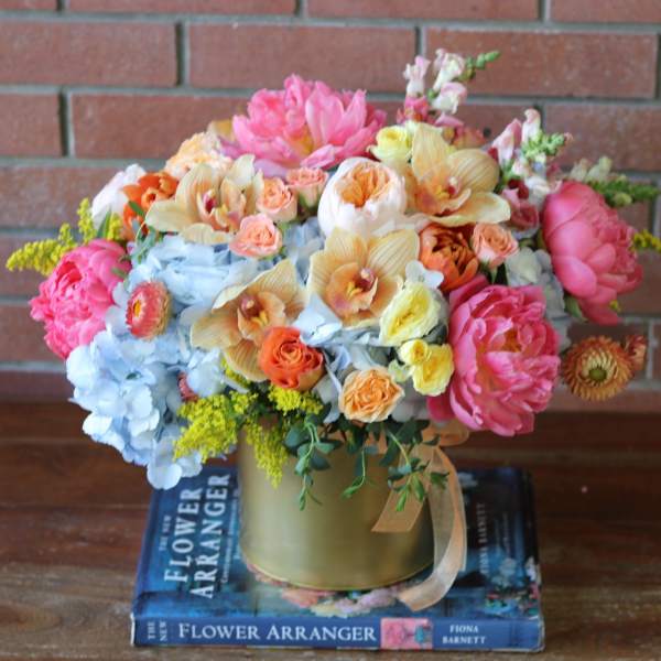 Colorful mixed flower arrangement in a gold vase on stacked books