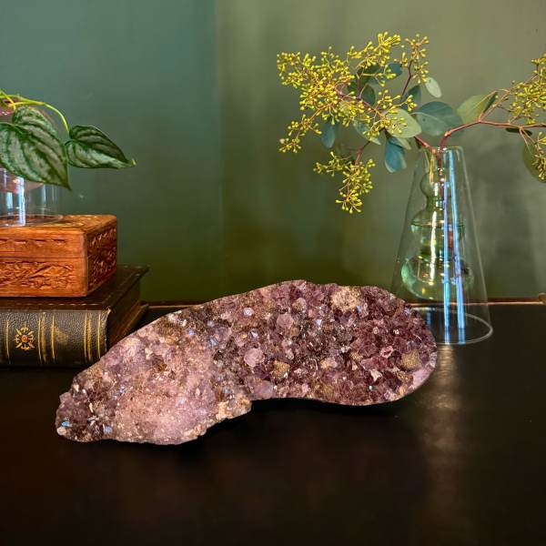 Amethyst crystal cluster on a dark surface with a glass vase and plant stems