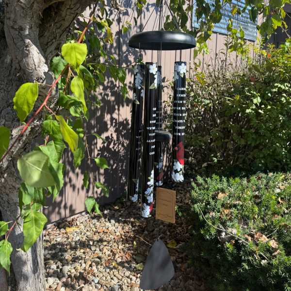 Black memorial wind chime hanging outdoors among trees and shrubs