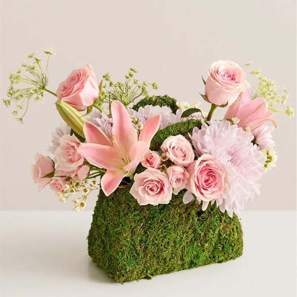 Pink roses and lilies arranged in a moss-covered container