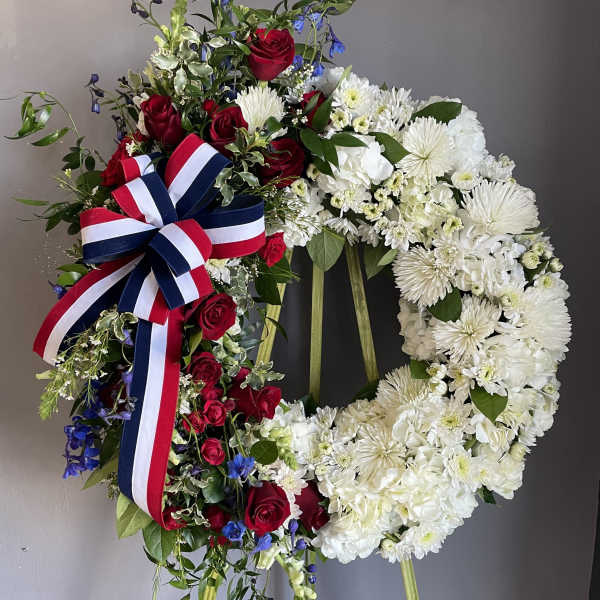 Two floral wreaths on stands, one red white and blue with roses and one white with chrysanthemums