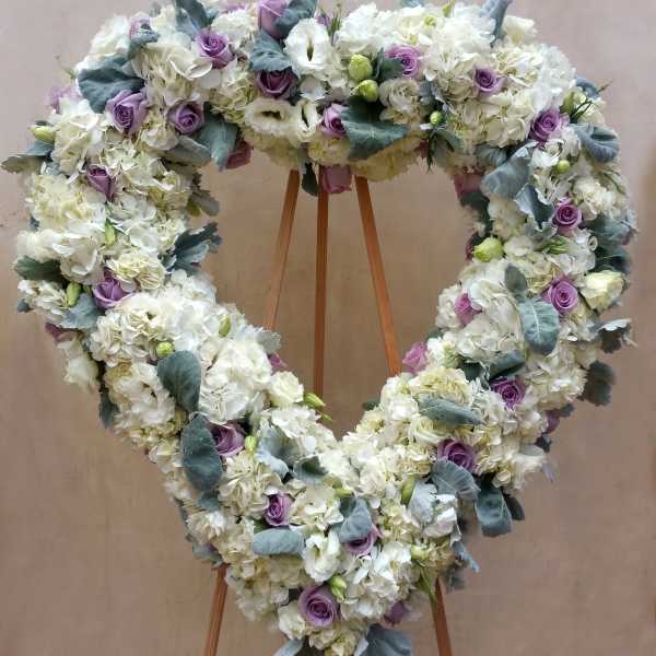 Heart-shaped floral wreath of white blooms and lavender roses on a stand