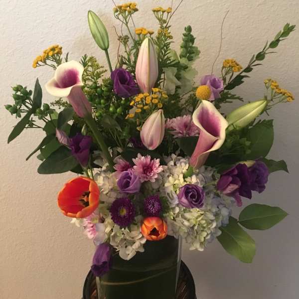 Mixed bouquet with purple flowers, calla lilies, and orange tulips in a vase