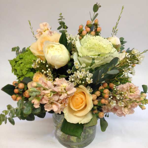 Low arrangement of peach and cream roses with mixed blooms in a clear glass vase