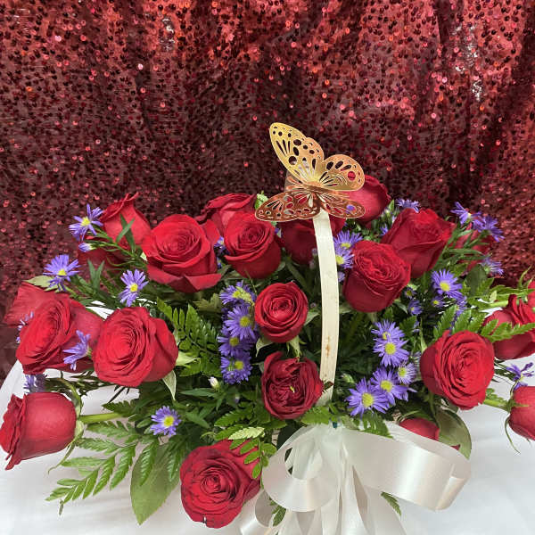 Red roses and purple daisies in a white basket with a butterfly topper