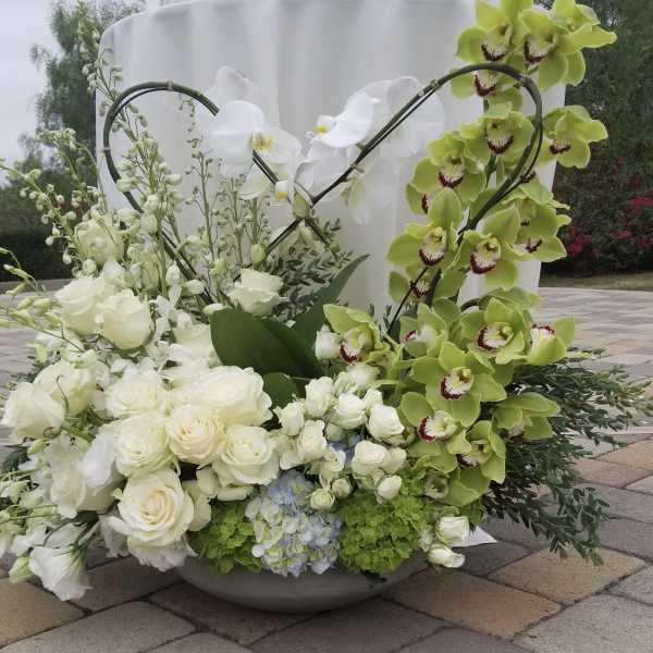 Large floral arrangement with white roses and green orchids in a low bowl