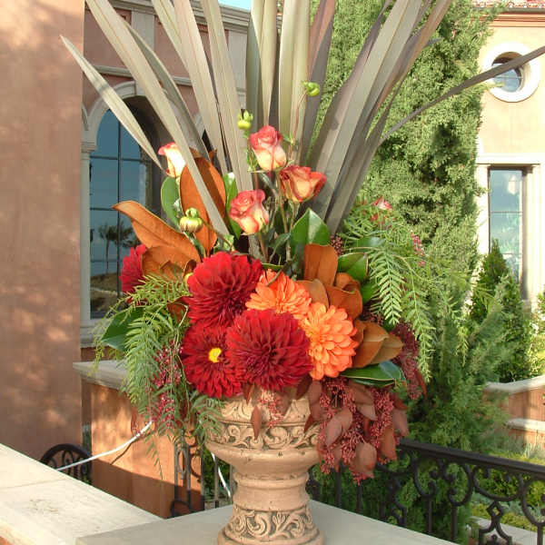 Tall urn arrangement with red and orange flowers and long spiky foliage