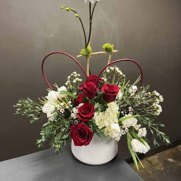 Red roses and white orchids in a white vase with heart-shaped accents