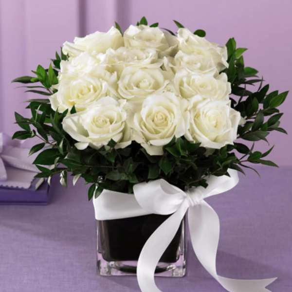 White roses in a square glass vase with a white ribbon