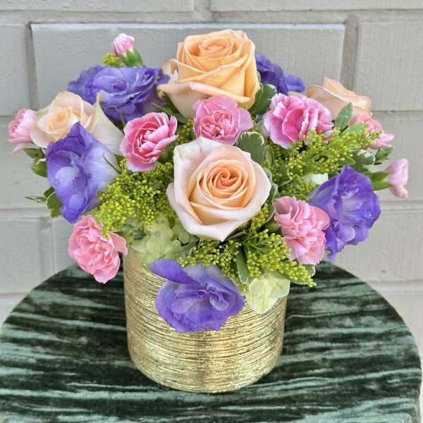 Peach roses, pink carnations, and purple lisianthus in a gold vase