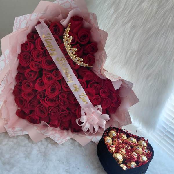 Bouquet of red roses with a birthday ribbon and tiara, plus a box of chocolates.
