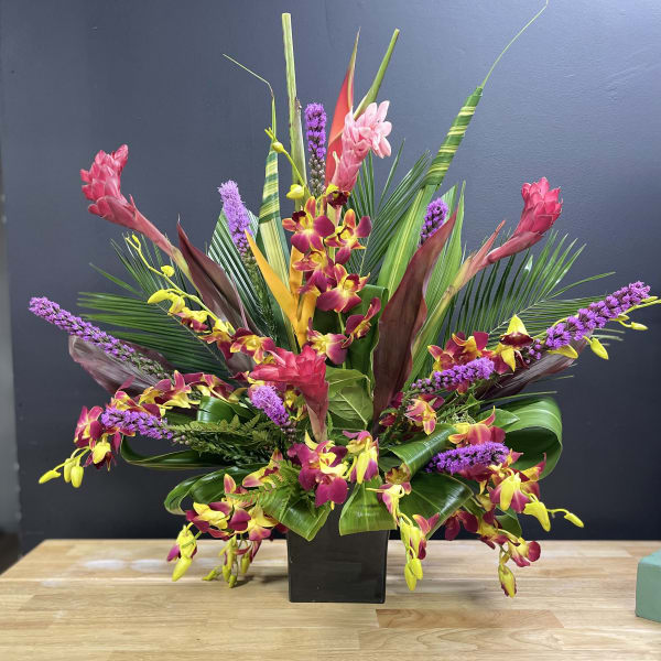Tropical floral arrangement with orchids and pink blooms in a black vase