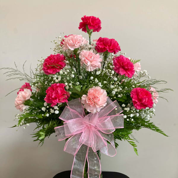 Pink and light pink carnations in a glass vase with a pink ribbon bow