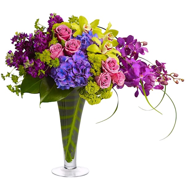 Colorful bouquet of roses, hydrangeas, and orchids in a tall glass vase
