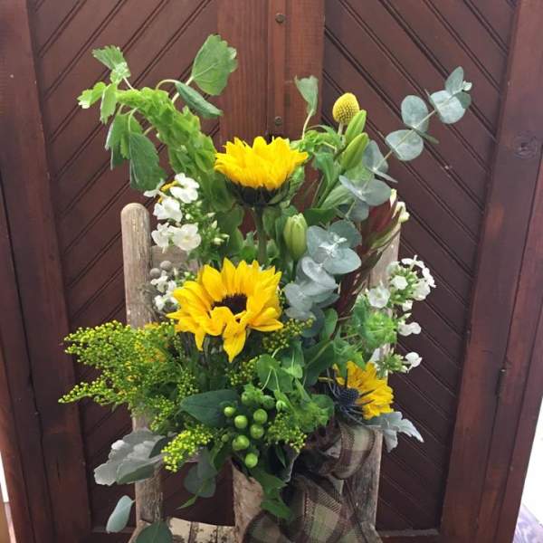 Tall bouquet with yellow sunflowers and mixed greenery in a rustic container