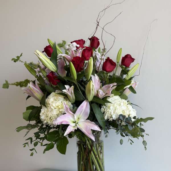 Tall bouquet of red roses, pink lilies, and white hydrangeas in a glass vase
