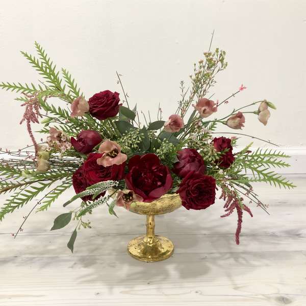 Deep red floral arrangement in a gold pedestal bowl