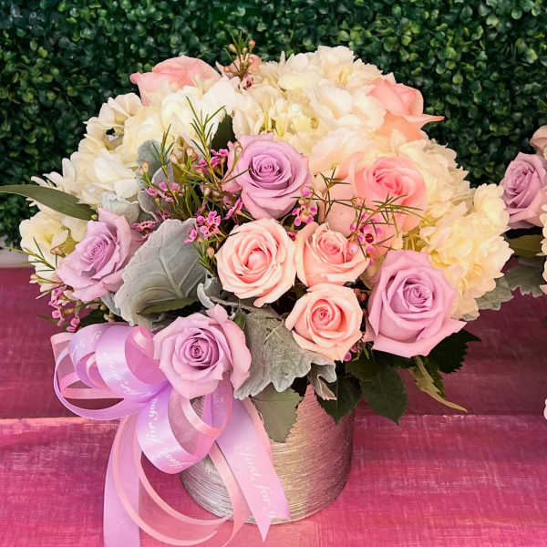 Pink and lavender roses in a round vase with a ribbon bow