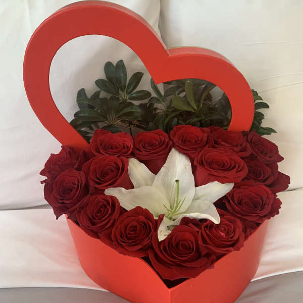 Red roses and a white lily arranged in a heart-shaped box