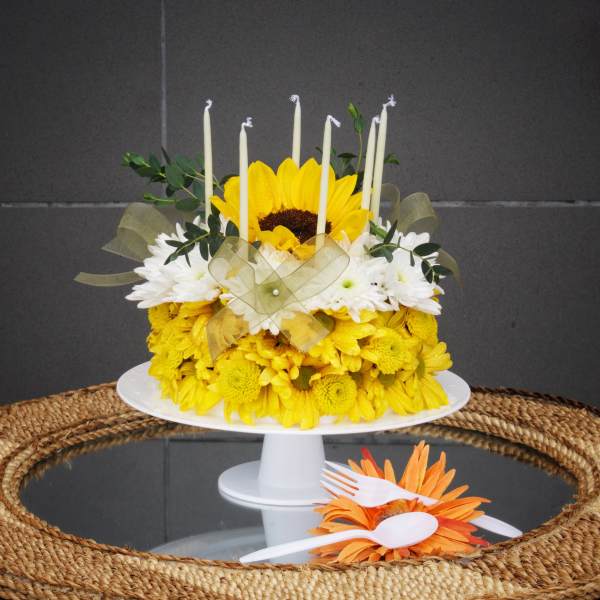 Yellow and white floral cake with candles on a white stand
