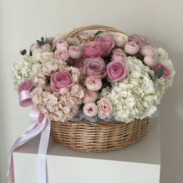 Pink roses and pale hydrangeas in a wicker basket with ribbon